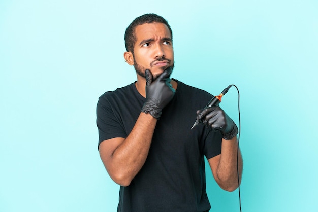 Tattoo artist Ecuadorian man isolated on blue background having doubts