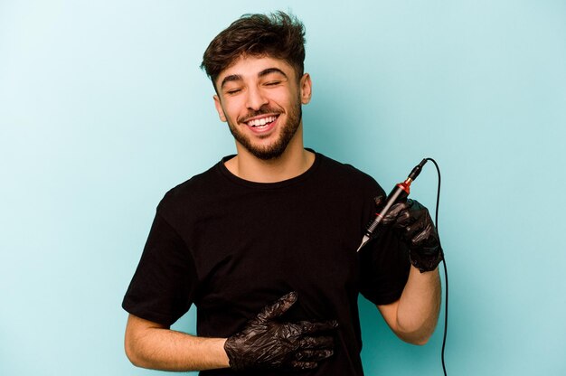 Tattoo artist hispanic man isolated on blue background laughing and having fun