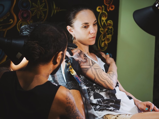 Photo tattoo artist making tattoo on hand of female customer