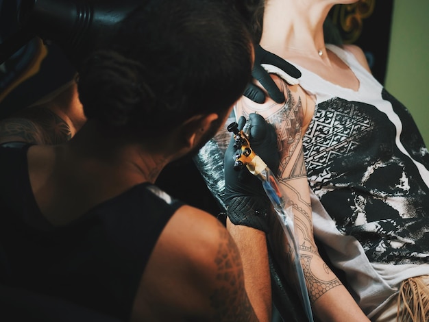 Photo tattoo artist making tattoo on hand of female customer