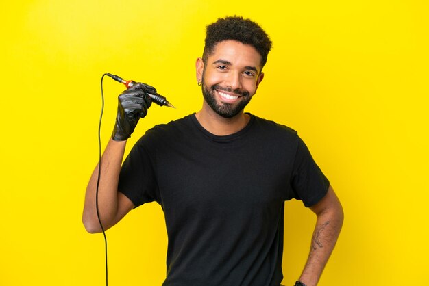 Tattoo artist man brazilian man isolated on yellow background posing with arms at hip and smiling