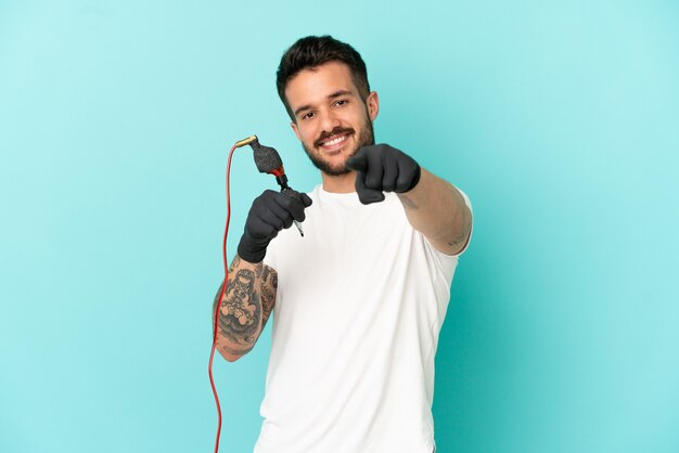 Tattoo artist man over isolated blue background points finger at you with a confident expression