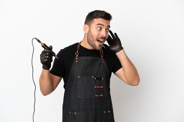 Tattoo artist man isolated on white background listening to something by putting hand on the ear