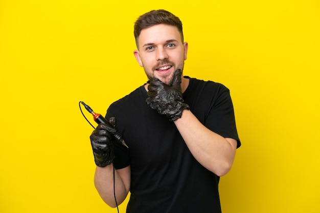 Tattoo artist man isolated on yellow background happy and smiling