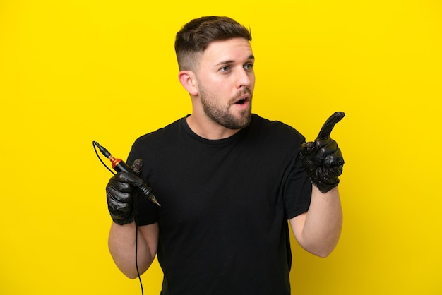 Tattoo artist man isolated on yellow background intending to realizes the solution while lifting a finger up