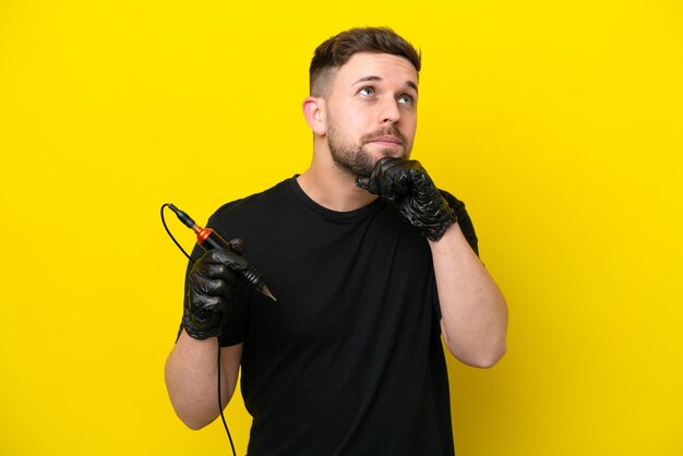 Tattoo artist man isolated on yellow background and looking up