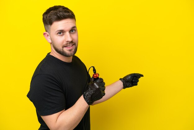 Tattoo artist man isolated on yellow background pointing back