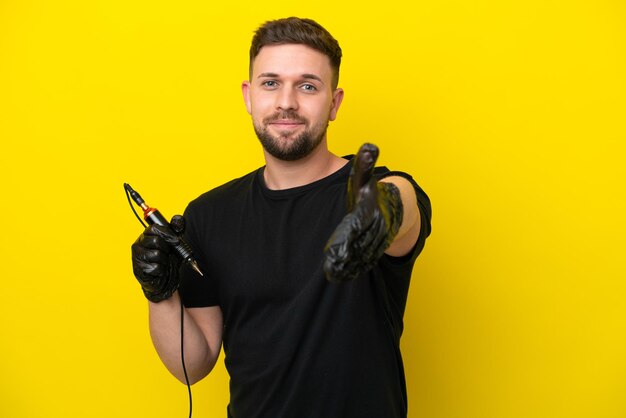 Tattoo artist man isolated on yellow background shaking hands for closing a good deal