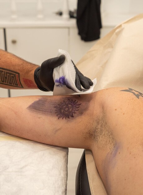 Фото Татуировщик выполняет татуировку на клиенте