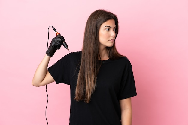 Tattoo artist woman isolated on pink background looking to the side