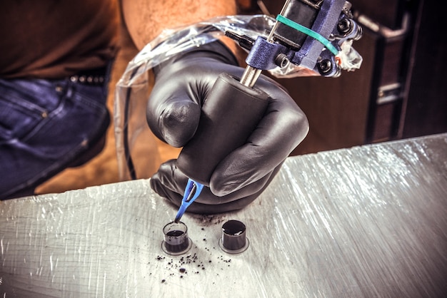 tattoo artist working with a tattoo machine with black gloves on and use a black inks for tattooing.