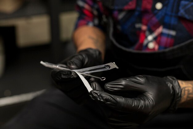 Tattoo artist39s hands removing the sterilized tattoo needle
from its container he is wearing black gloves body art concept