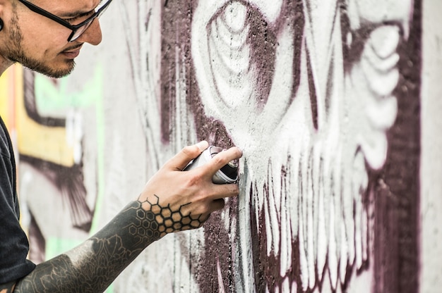 Tattoo graffiti schrijver schilderij met kleur spray zijn donkere foto op de muur. Hedendaagse kunstenaar aan het werk