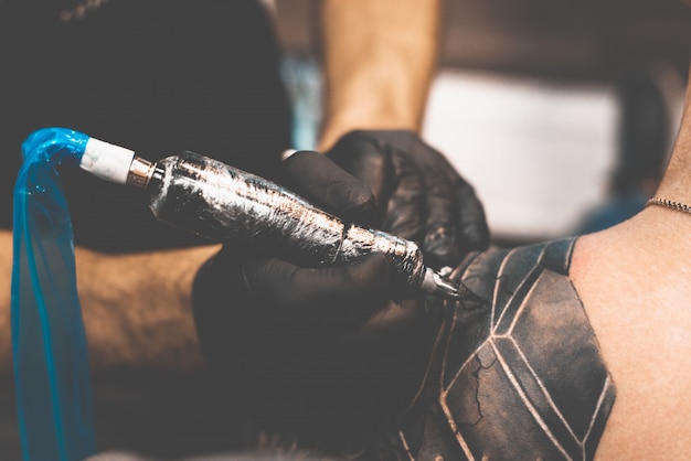 Tattoo salon. The tattoo master is tattooing a man on his shoulder. Tattoo machine, safety and hygiene at work. Close-up, tinted, tattooist