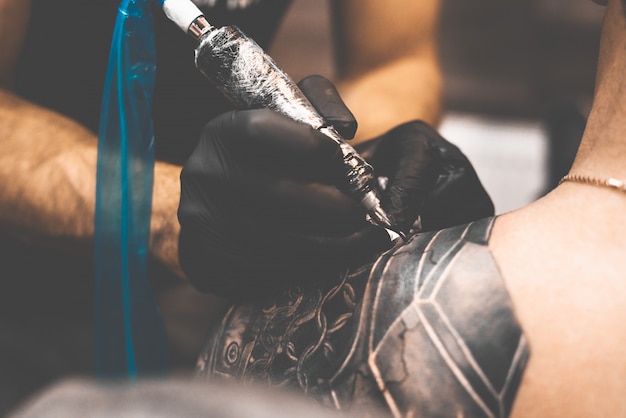 Tattoo salon. The tattoo master is tattooing a man on his shoulder. Tattoo machine, safety and hygiene at work. Close-up, tinted, tattooist