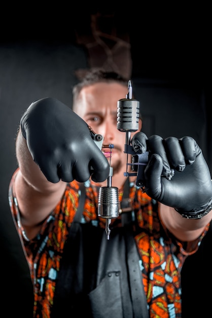 Tattoo specialist poses with tattoo machine in tattoo studio.