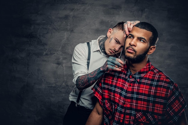 Tattooed barber cuts the beard to a Black bearded male.