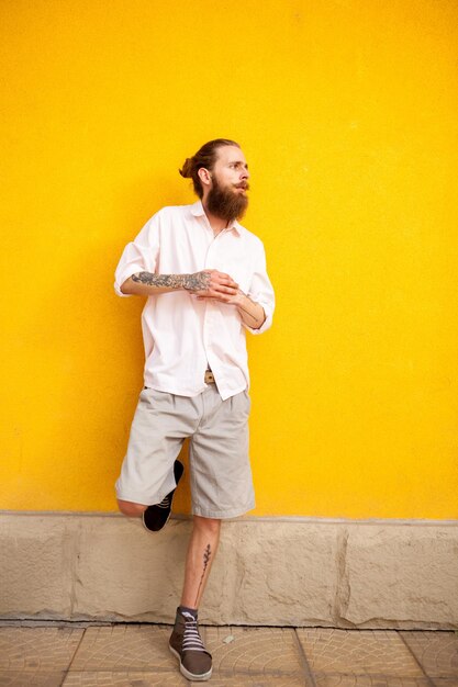 Tattooed bearded attractive man on yellow wall posing outdoor