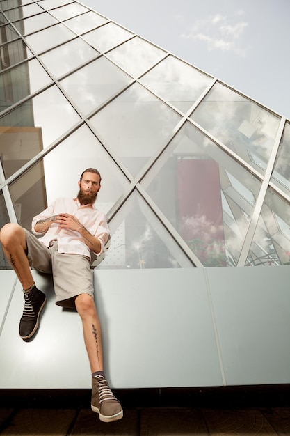 Tattooed and bearded hipster in front of office building posing cool at camera