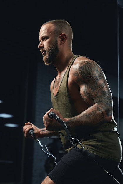 Tattooed bodybuilder doing low cable crossover exercise.