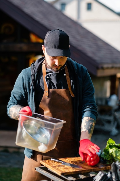 Tattooed chef lays out food for cooking juicy steak and vegetables outdoors