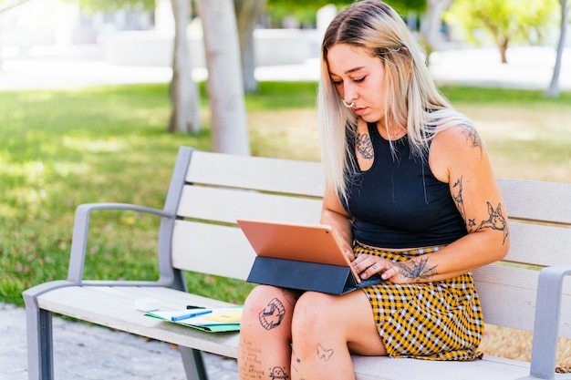 Tattooed college girl studying with a tablet on campus