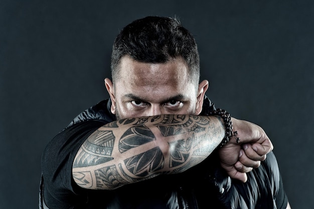 Photo tattooed elbow hide male face dark background. visual culture concept. tattoo can function as sign of commitment. do tattoos hide lack of masculinity. man brutal guy cover face with tattooed arm.