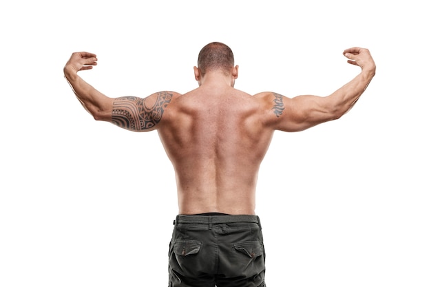 Tattooed male bodybuilder posing over white wall. Fitness workout