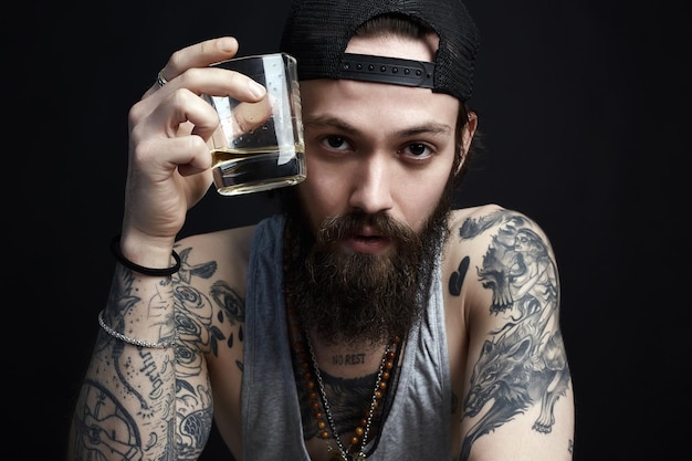 Tattooed man in hat drinking a whiskey