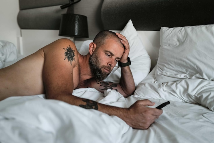 Photo tattooed man laying in bed using phone