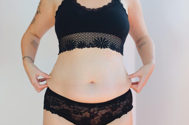 Tattooed woman in black underwear with fat belly, overweight female body isolated. white background