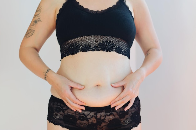 Tattooed woman in black underwear with fat belly, overweight female body isolated. white background