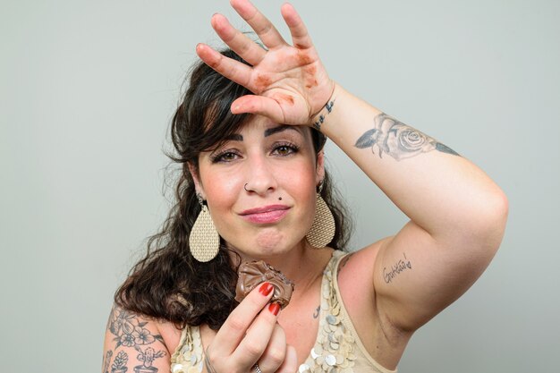 Tattooed woman, looking with her hand on her head and sorry that she ate a Brazilian honey cake. Tattoo on left biceps written in Portuguese - Gratitude.