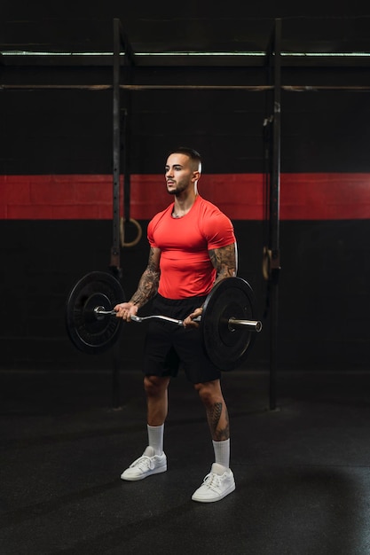 tattooed young guy doing sports in a gym with weights and rowing machine