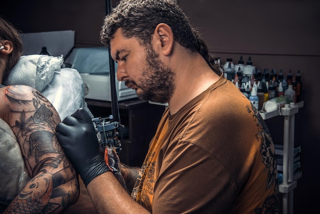 Tattooer doing tattoo in salon./Professional tattoo artist works in tattoo studio.