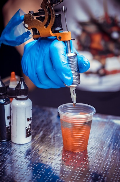 A tattooer, holding in his hand, a tattoo gun.