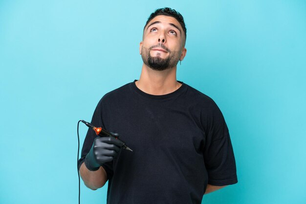 Tattooist arab man isolated on blue background and looking up