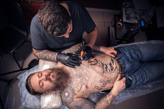 Tattooist makes a tattoo on the skin in tattoo parlor.