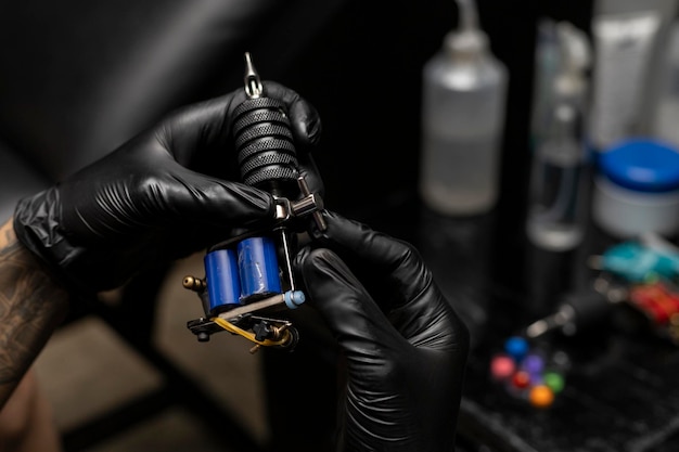 Tattooist setting up and adjusting his tattoo machine wearing\
black gloves body art concept