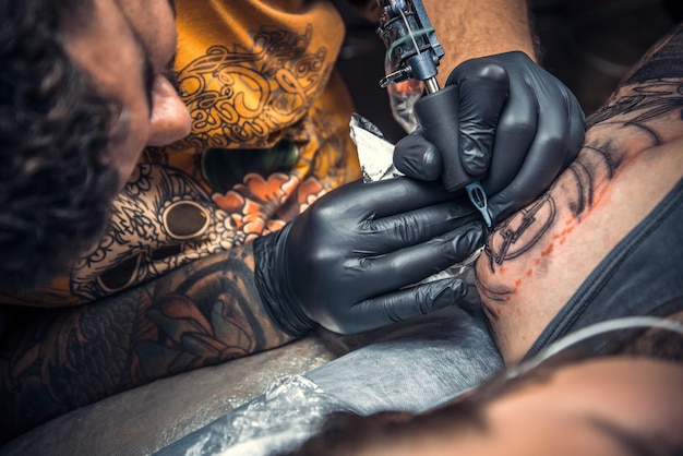 Tattooist showing process of making a tattoo in tattoo studio./Professional tattooist create tattoo in tatoo salon.