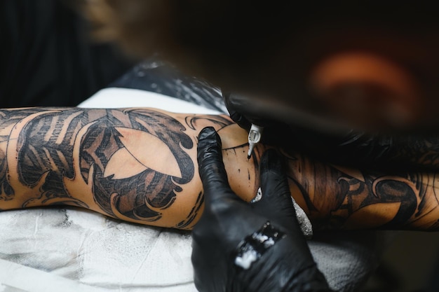 Tattooist with his machine tattooing on the arm with the design drawn, concept of art and design