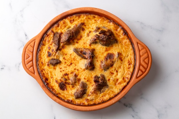 Photo tave kosi is a national albanian dish of baked lamb and rice with yoghurt close-up in a pan on the table. horizontal top view from above. turkish name; elbasan tava