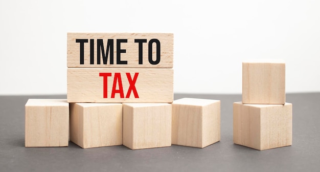 税の概念税の言葉は、灰色の背景の木製の立方体に書かれています木製の要素のクローズアップ背景には、浴槽の税の時間の緑の花です
