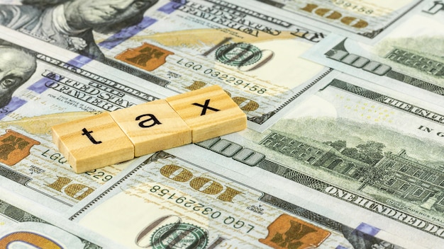 Tax Concept with wooden block on dollar bills.