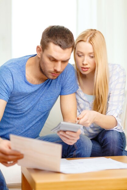 Photo tax, finances, family, home and happiness concept - busy couple with papers and calculator at home