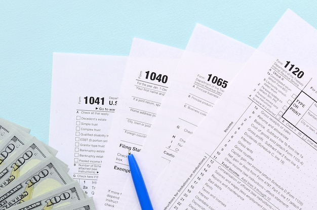 Tax forms lies near hundred dollar bills and blue pen on a light blue background Income tax return