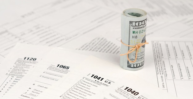 Tax forms lies near roll of hundred dollar bills