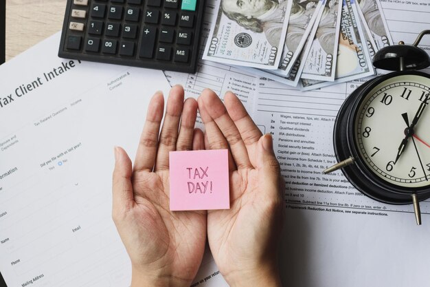 Tax forms with calculator money alarm clock and tax day written on a sticky note