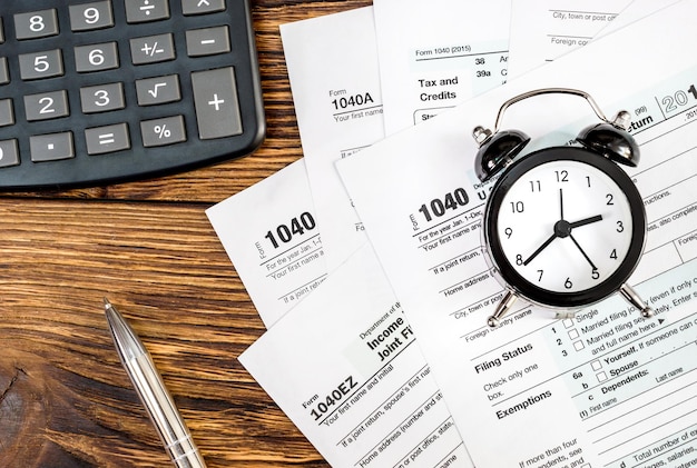 Tax forms with clock pen and calculator on the office wooden table Top view Business and tax concept