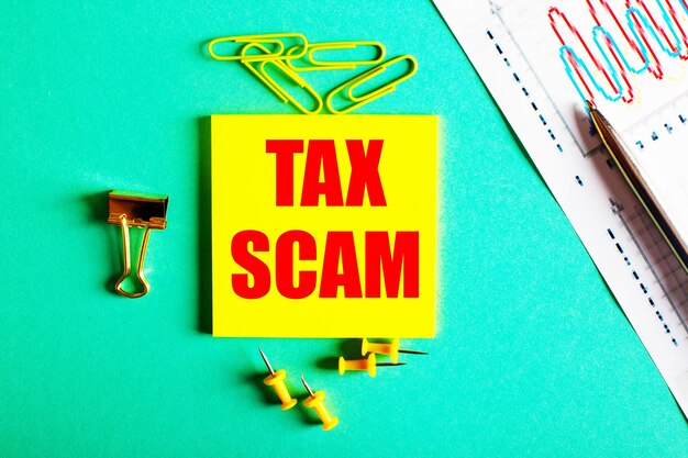 TAX SCAMは、グラフと鉛筆の近くの緑のテーブルの黄色のステッカーに赤で書かれています